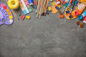 Flat lay composition with different paints, brushes and color palette on grey background. Space for...
