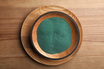 Bowl with spirulina powder on wooden background, top view