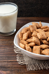 Dried breakfast pads in white bowl and milk on dark wooden background.