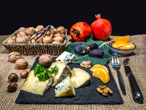 The peaces of the French cheese named Tommete des Alpes, nuts and walnuts with mandarin, date fruit and pomegranates on the natural stone plate for vegetarians as health food.