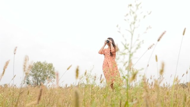 A beautiful girl walks through the field. Photographing landscapes. Long hair. Slow shooting. Slim brunette in a dress