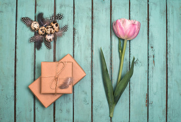 Easter eggs decoration on rustic wooden background. Quail  eggs, gift box and pink tulip on a old wooden background. Vintage style picture.