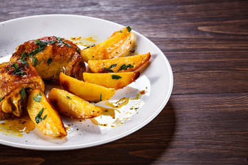 Grilled chicken thighs with baked potatoes on wooden table