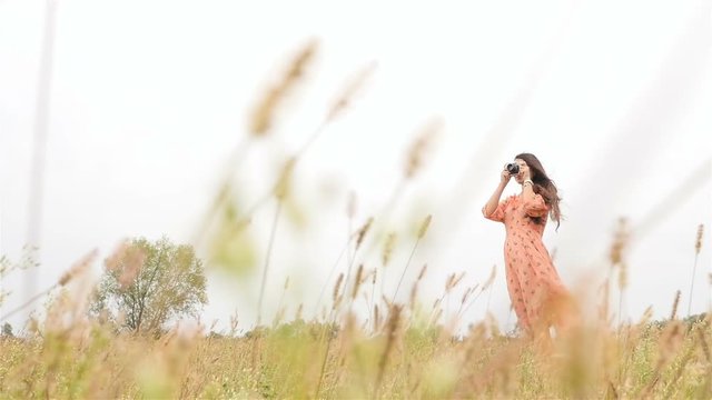 Beautiful brunette with a camera. Dress develops in the wind. Slow motion. Green grass