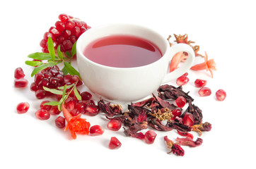 Parts of a pomegranate with pomegranate seeds and leaves, flowers, dry tea of carcade and full cup of tea isolated on white background