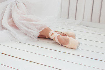 Young woman authentic ballerina ballet dancer in pointe shous sitting on white floor