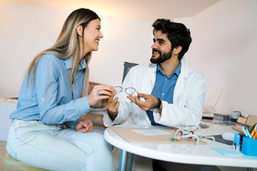 Obraz premium Woman choosing her new glasses at optics store with help of ophthalmologist