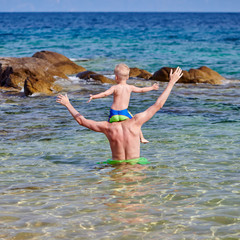 Toddler boy on father's shoulders at beach
