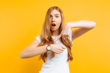 beautiful girl looking at a hand watch, points to the watch, on a yellow background, concept of being late