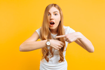 beautiful girl looking at a hand watch, points to the watch, on a yellow background, concept of...