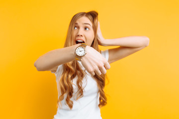beautiful girl looking at a hand watch, points to the watch, on a yellow background, concept of...
