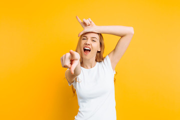 girl shows the gesture of a loser or loser, in a white t-shirt with a grin on his face, on a yellow...