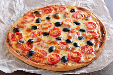 Homemade pizza with tomato and olives on paper over