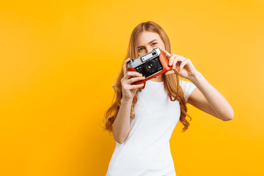beautiful girl with a camera in her hands, on a yellow background