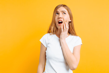Young sad girl is having a toothache, on yellow background