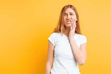 Young sad girl is having a toothache, on yellow background