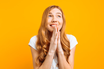 focused girl asks God to help her, holding hands near her face, wishes good luck, on a yellow background