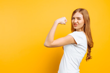 of happy girl in white t-shirt showing arm muscles on yellow background.