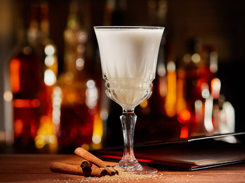 White cocktail with cinnamon on a bar counter with colorful bokeh background
