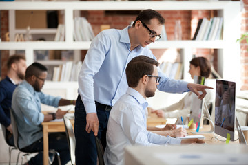 Executive manager helping male colleague with computer task in office