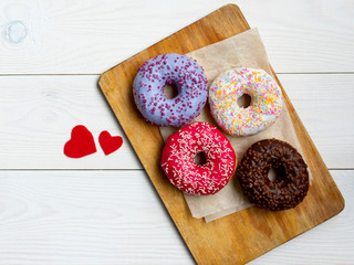 four assorted donuts lying on a wooden cutting board on white background