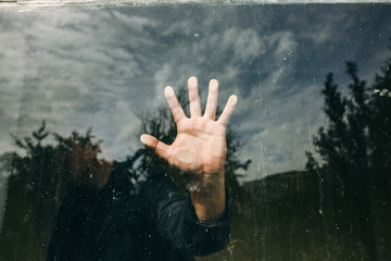 Man is holding hand on the glass window. Reflection of a guy with a nature on background. Lifestyle concept.