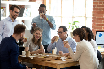 Multi-ethnic employees group enjoy takeaway food friendly conversation in office