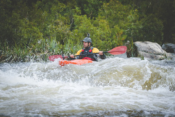 Close up image of a white water kayak paddler riding white water on a mountain river