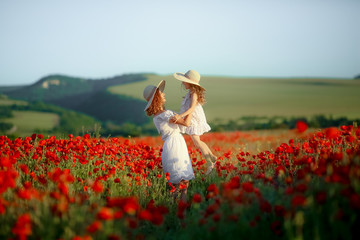 Mother and daughter in light dresses and hat walking on the farm field. Field of blooming poppies.