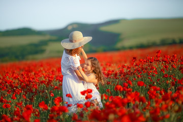 Mother and daughter in light dresses and hat walking on the farm field. Field of blooming poppies.