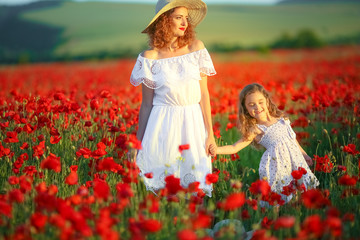 Fototapeta na wymiar Mother and daughter in light dresses and hat walking on the farm field. Field of blooming poppies.