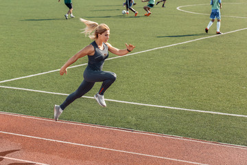 Sporty Lifestyle. Young woman on stadium near football game running motivated side view