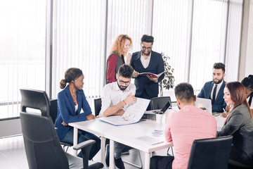Red-haired woman boss and her Indian male assistant leading corporate team meeting presenting team goals at well- lit conference room