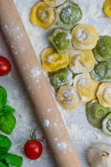 Homemade fresh Italian ravioli pasta on white wood table  with flour, basil, tomatoes,background,top view.
