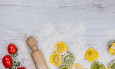 Homemade fresh Italian ravioli pasta on white wood table  with flour, basil, tomatoes,background,top view.