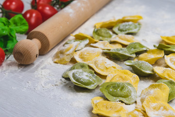 Homemade fresh Italian ravioli pasta on white wood table  with flour, basil, tomatoes,background