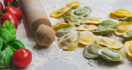 Homemade fresh Italian ravioli pasta on white wood table  with flour, basil, tomatoes,background