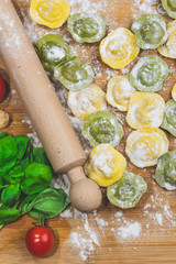 Homemade fresh Italian ravioli pasta on wood table  with flour, basil,tomatoes,background,top view.