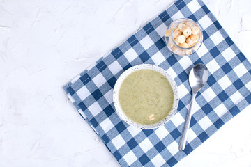 Cream soup puree with broccoli, cream and crackers. Lunch of vegetables on a light background. Plate and napkin on the table. Above.