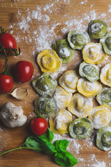 Homemade fresh Italian ravioli pasta on wood table  with flour, basil,tomatoes,background,top view.