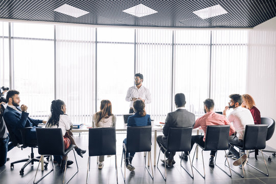 Achieving Best Results After Annual Refresher Course. Indian Young Business Mentor Conducting A Business Training While Standing In Front Of People Sitting In Row At Meeting Room.