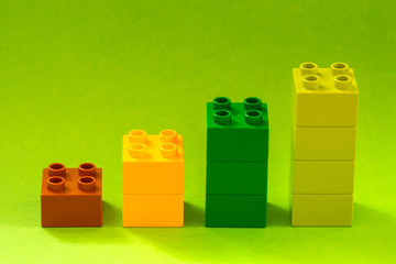 Growing bar chart from color toy blocks on green background.