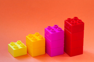 Growing bar chart from color toy blocks on red background.