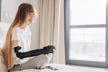 pale cheerful girl wearing a cyber hand sitting near the window in the clinic. copy...