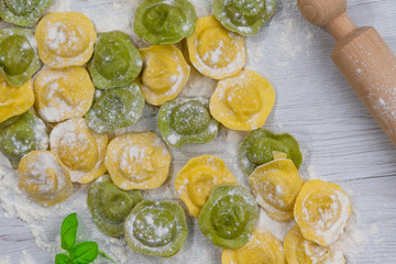 Homemade fresh Italian ravioli pasta on white wood table  with flour, basil, tomatoes,background,top view.