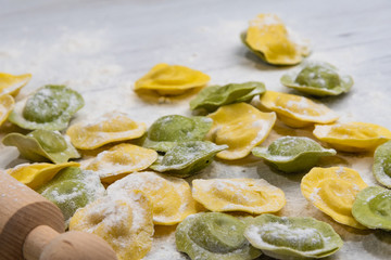 Homemade fresh Italian ravioli pasta on white wood table  with flour, basil, tomatoes,background