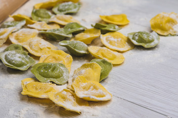 Homemade fresh Italian ravioli pasta on white wood table  with flour, basil, tomatoes,background