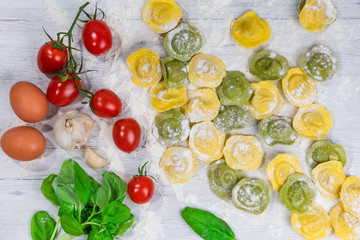 Homemade fresh Italian ravioli pasta on white wood table  with flour, basil, tomatoes,background,top view.