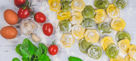 Homemade fresh Italian ravioli pasta on white wood table  with flour, basil, tomatoes,background,top view.