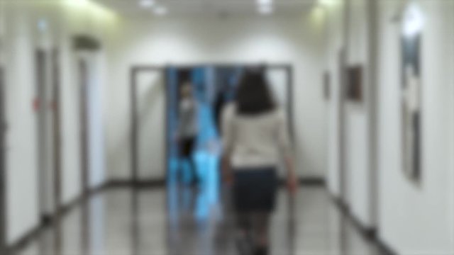 People walking down the hallway of a modern office building, blurred background.
